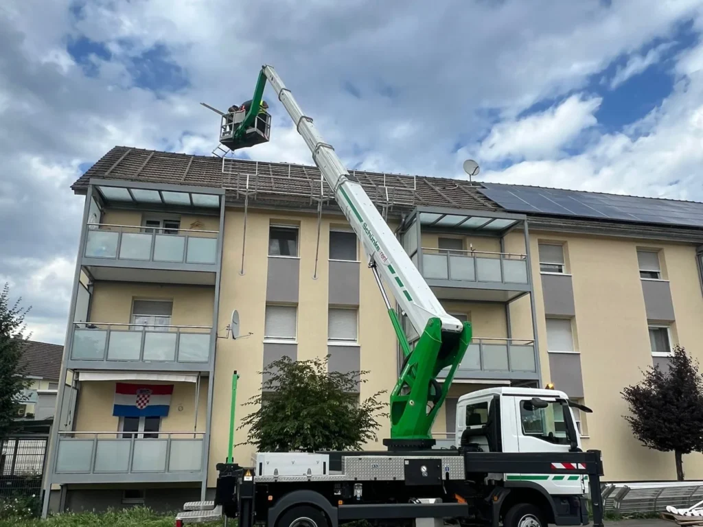 Hubsteiger vor einem Mehrfamilienhaus für Montagearbeiten am Dach