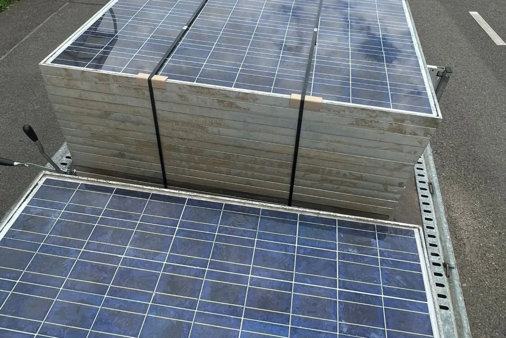 Gebündelte Solarmodule mit Spanngurten auf einer Ladefläche, ein weiteres Modul liegt davor